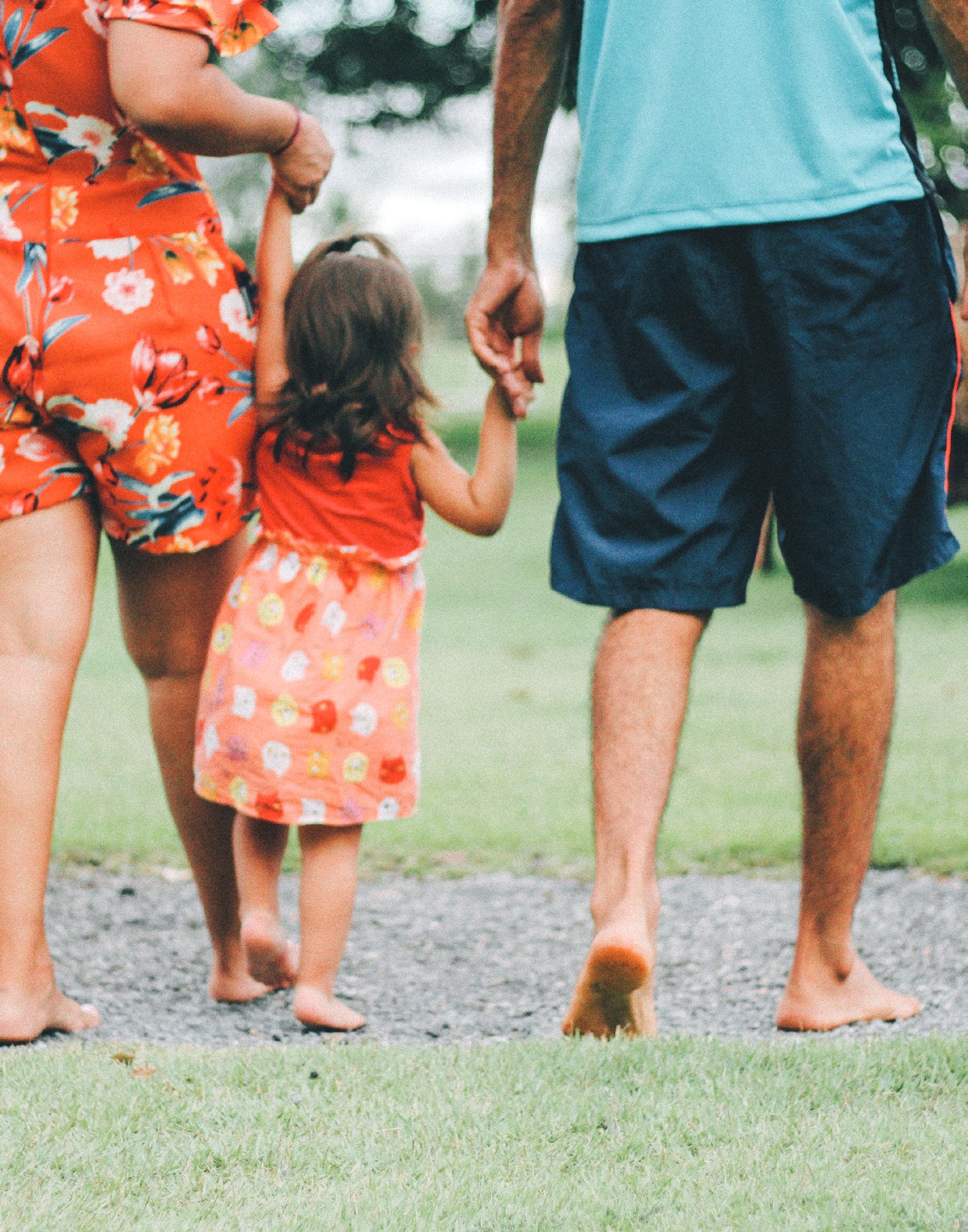 An adult and a child walking hand in hand across grass