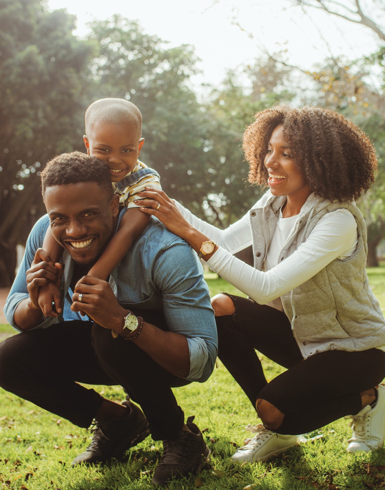 Two adults and a child smiling together outdoors in a park